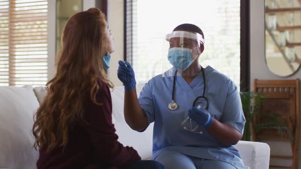 African american female doctor wearing face mask giving covid swab test to female patient