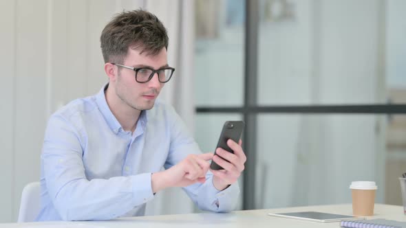 Young Man Celebrating Success on Smartphone in Office