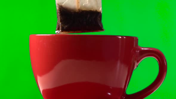 Wet Tea Bag Over Ceramic Red Cup Isolated on Green Background