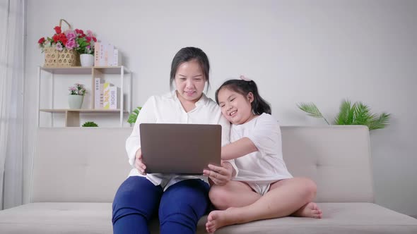 Mom and kid having fun laughing and watching Korea Drama series on laptop together in living room