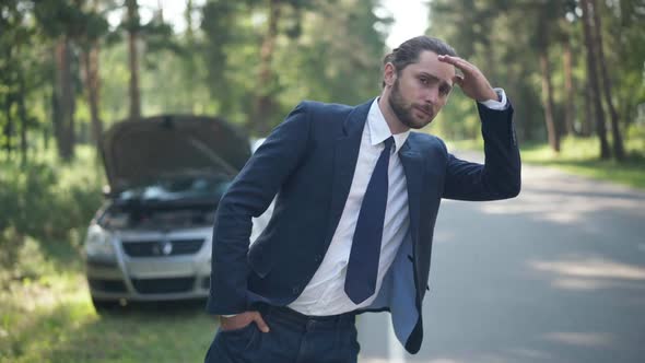 Medium Shot Portrait of Anxious Caucasian Man with Broken Car Waiting for Help Standing in Sunlight