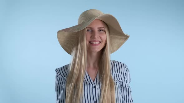 Beautiful Smiling Girl Putting a Hat on Her Head on Blue Background