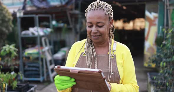 Mature african woman working inside greenhouse garden using digital tablet - Nursery and spring conc