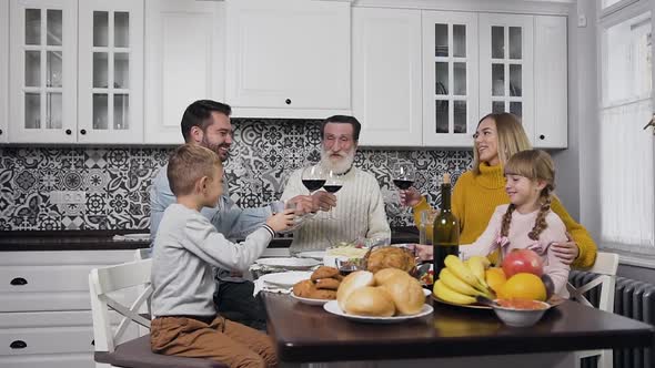 Family Celebrating Thanksgiving Day with Raised Glasses Sitting at the Festive Kitchen Table