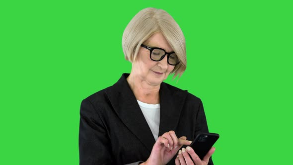 Beautiful Mature Woman in Eyeglasses Using a Smartphone on a Green Screen Chroma Key