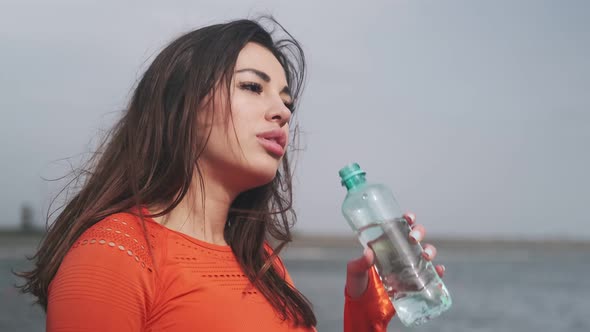 Athletic fitness woman, sportswoman drinks water. Attractive sports girl drinks water on the street