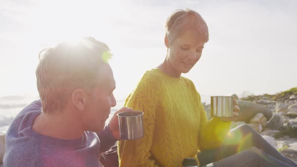 Caucasian couple enjoying free time by sea on sunny day drinking coffee