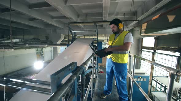 Male Worker with a Laptop is Observing Paperproducing Machine