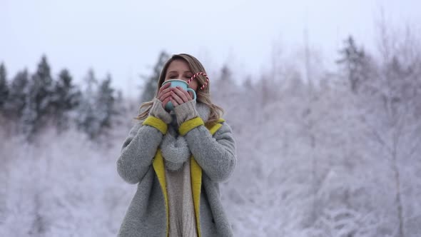 Beautiful woman in coat with cup of hot drink in a snow forest.