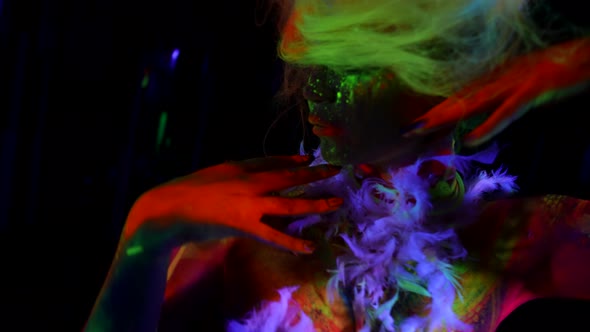 Mysterious Woman with Neon Fluorescent Paints on Face and Body Glowing Hair in UV Lights
