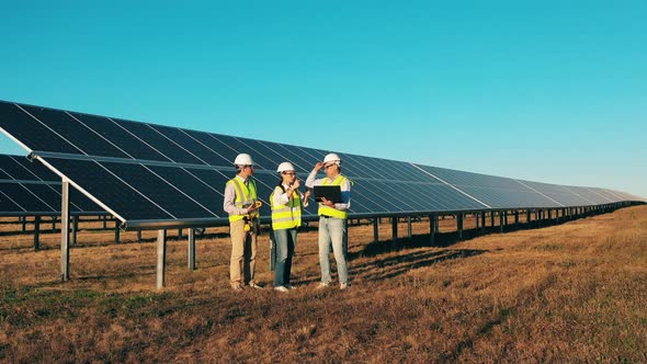 Drone Shot of Three Solar Energy Specialists Having a Discussion at a Solar Power Plant