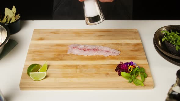 Professional Chef Adding Salt on Raw White Fish Fillet on Cutting Board Closeup Thin Slice