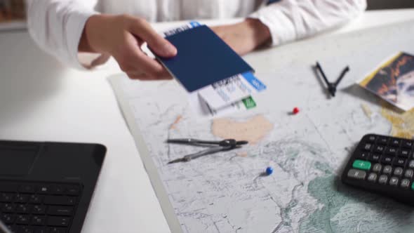 Young Woman Agent In Travel Agency Holds Out Passport, Tickets. There Is Map, Laptop, Calculator