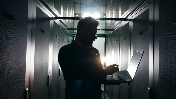 Dark Server Unit with an IT Specialist Operating a Laptop. IT Engineer Working in a Server Room.