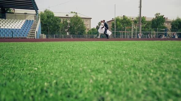 Bride and Groom are Running Along the Treadmill at the Stadium the Green Grass