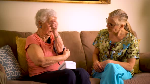 Home healthcare nurse and elderly woman taking blood pressure with a monitor.