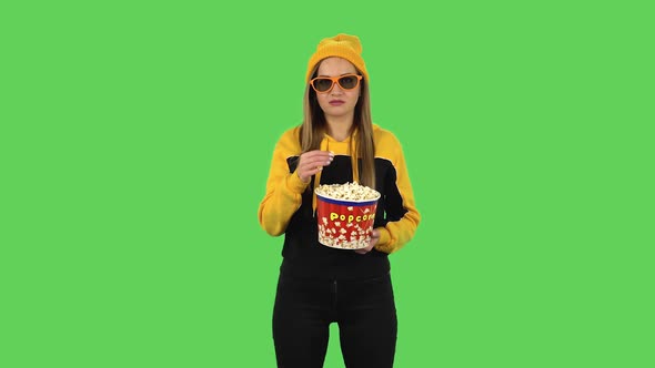 Modern Girl in Yellow Hat in 3D Glasses Is Watching a Boring Movie and Eating Popcorn. Green Screen