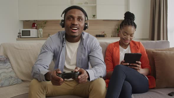 Happy African American Couple Chilling at Home on a Couch Surfing on a Tablet and Playing Console