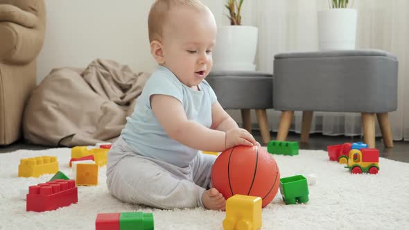 Cheerful Baby Boy Playing and Having Fun with Basketball on Floor at Living Room