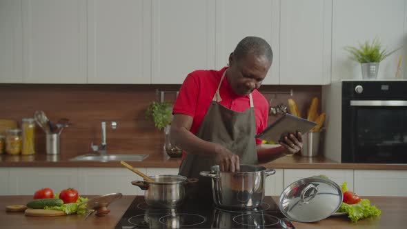 Elderly Male in Kitchen Preparing Food Using Tablet Pc