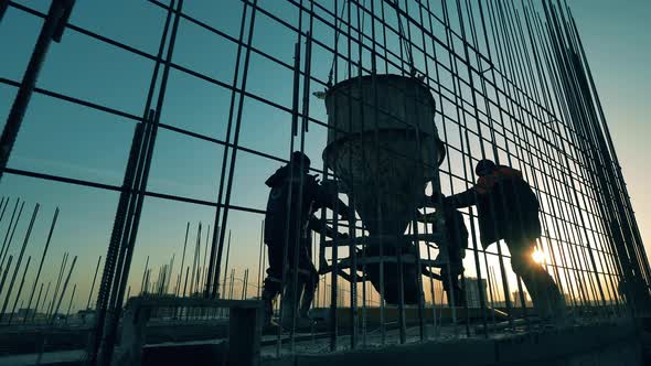 Construction Workers Watch a Crane Moving Concrete Container. alt
