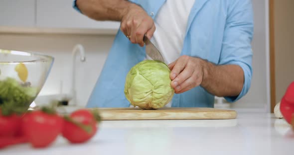 Male Well-Maintained Hand which Cutting Green Cabbage on Two Parts Using Knife on Cutting Board 