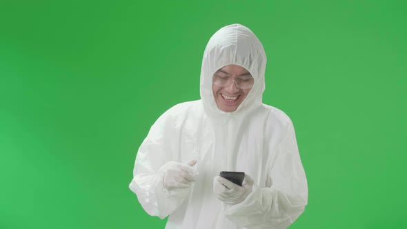 Happy Asian Man Wear Protective Uniform Ppe And Use Mobile Phone In The Green Screen Studio