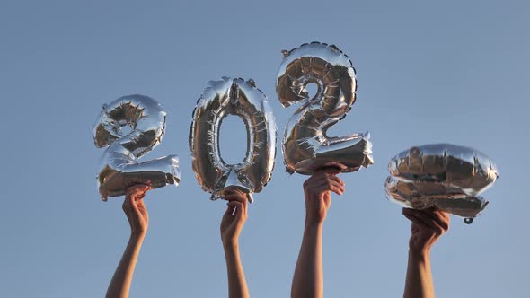 Hands Raise Up Balloons in the Form of Numbers 2022 Against the Blue Sky