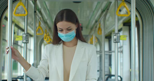 Portrait of Young Woman Wearing Medical Face Mask Rides in Tram, Holds Handrail, Protecting Against