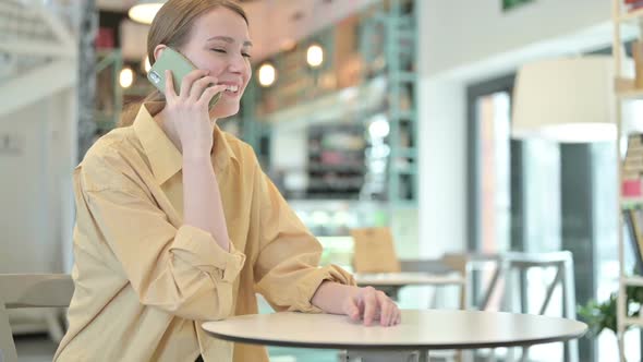 Cheerful Young Woman Talking on Smartphone in Cafe