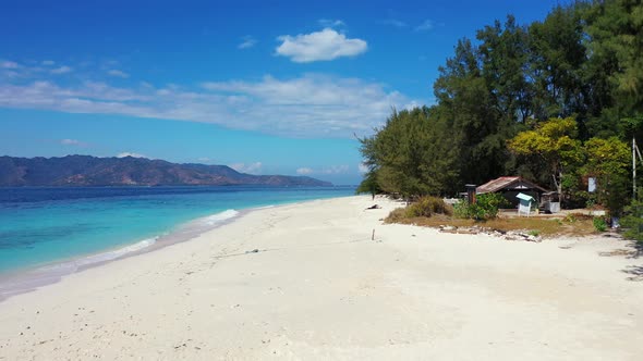 Pristine exotic beach with white sand under shadow of tall trees, washed by blue azure sea on a brig