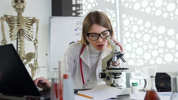  Young Doctor in Glasses Working with Microscope and Computer in the Clinic Cabinet