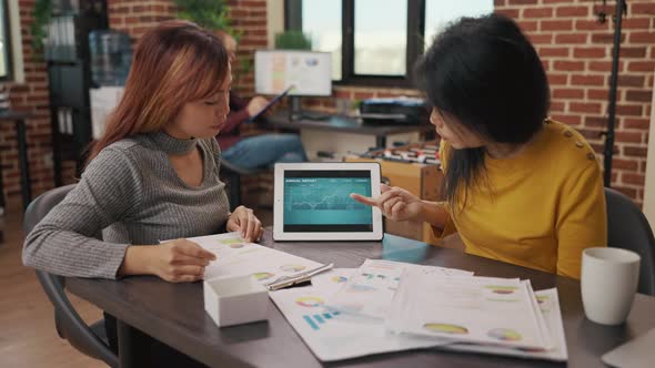 Business Women Examining Financial Charts on Digital Tablet and Papers