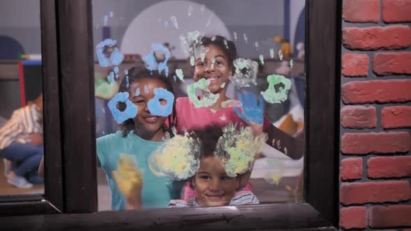 Smiling Children Waving Painted Palms at Window