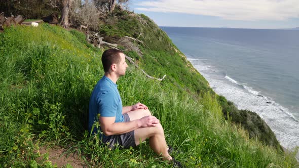 A fit strong man sitting in a meditating pose while doing deep breathing exercises on the edge of a