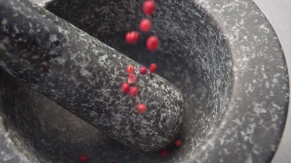 Closeup of the Red Peppercorns are Falling Into the Grey Stone Mortar