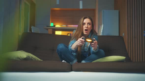 A Beautiful Excited Young Gamer Girl is Sitting on a Couch and Playing Video Games on a Console