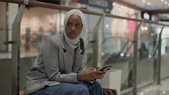 Black Woman with Hijab and Cellphone Rests in Trade Mall