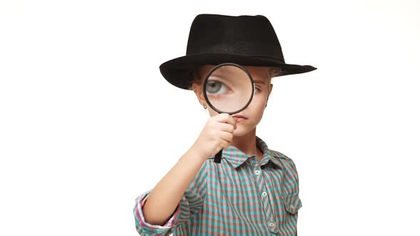 Small Serious Caucasian Kid Girl in Plaid Shirt and Black Hat Looking Through Magnifying Glass on