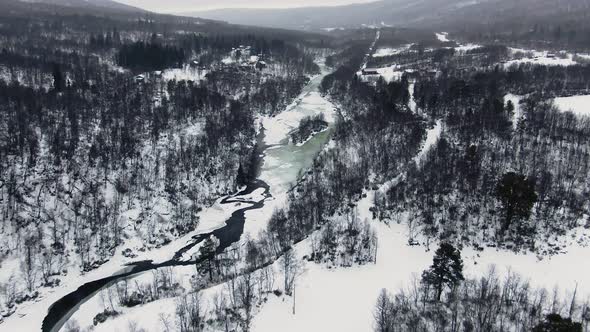 Wide panoramic aerial tilt from snowy forest and mountains to icy lake