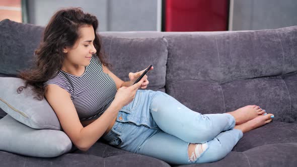 Happy Relaxed Young Homely Woman Enjoying Chatting Using Smartphone Lying on Couch