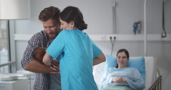 Nurse Giving Newborn Son Wrapped in Blanket to Young Father in Hospital