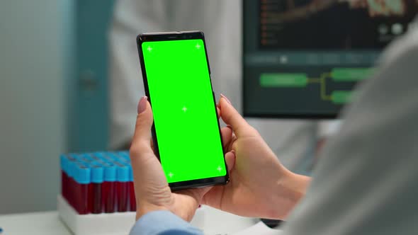 Close Up of Doctor Holding Phone with Green Screen Sitting at Desk