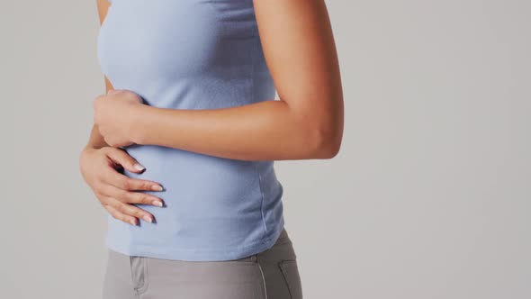 Video of biracial woman touching her stomach on white background