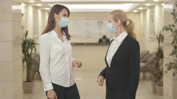 Two Businesswomen in Face Masks Touching Elbows Instead of Handshake in Business Center Hall