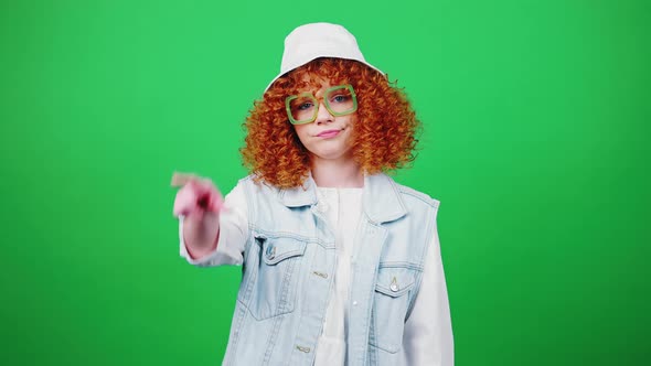 Young Displeased Redhead Curly Lady in Eyeglasses and Panama Hat Showing Loser Hand Gesture Green