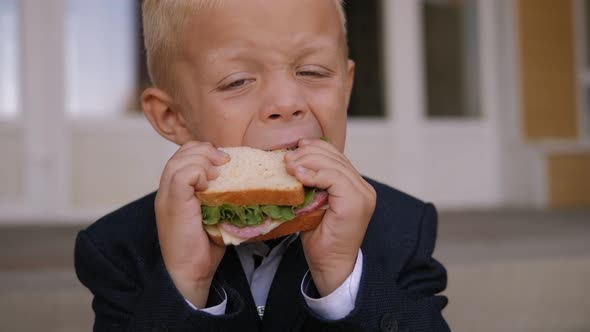 Schoolboy in a Jacket Eats a Sandwich in the Schoolyard Sitting on the Stairs