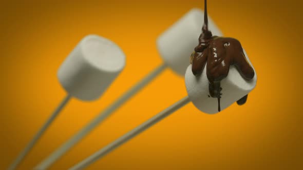 Chocolate Sauce Pouring Over Marshmallows on Warm Orange Background. Summer Time Concept. Close-up