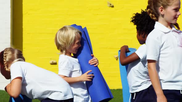 School kids holding yoga mat and interacting with each other