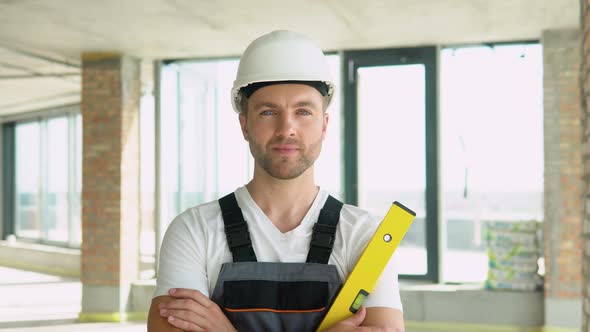 Portrait of an Engineer in a Helmet with Yellow Balance Ruler at a Construction Site